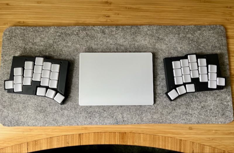 TOTEM split keyboard with white keys and black case on a grey felt desk mat with an Apple keyboard between the halves