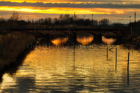 sunset on river under  ancient railway bridge