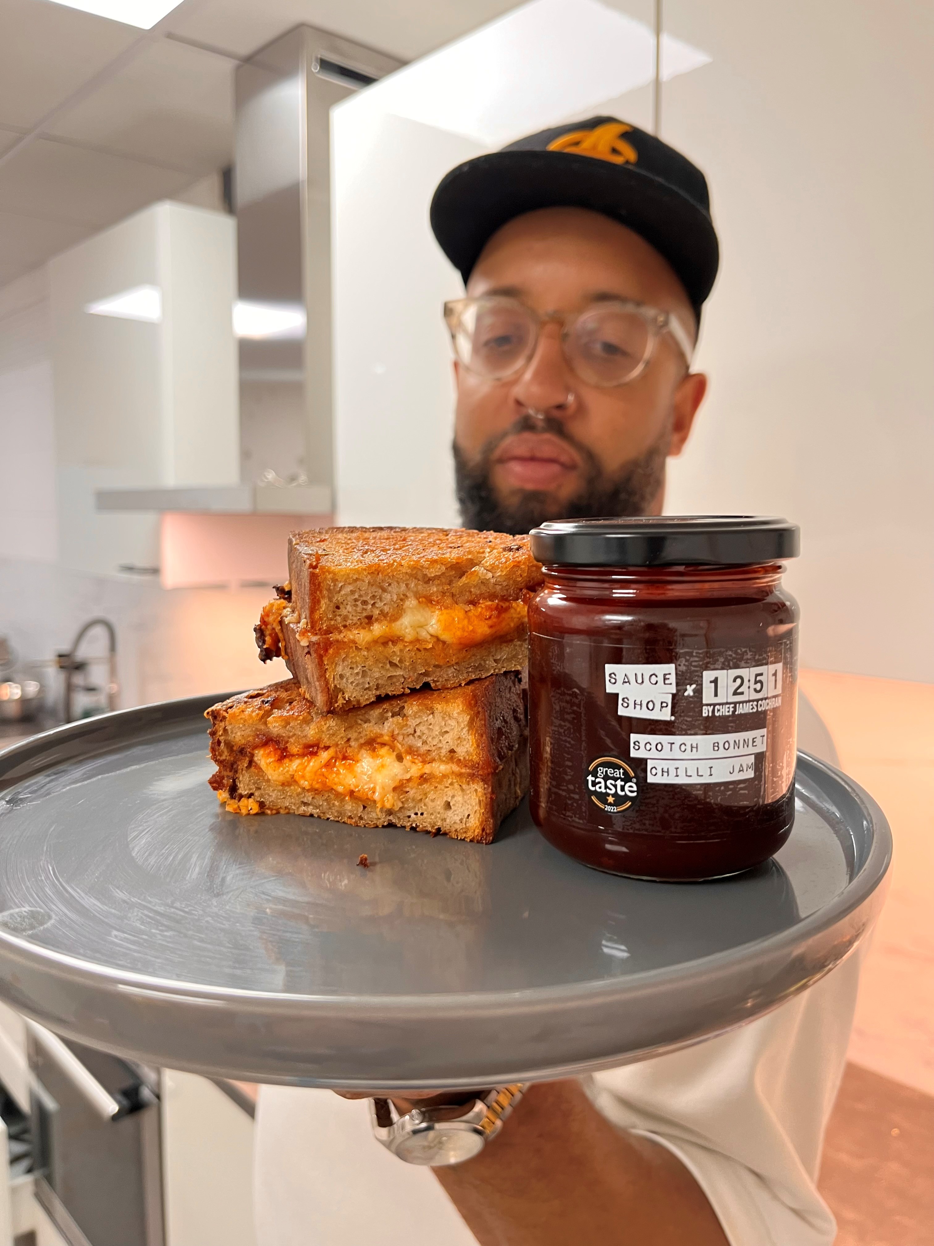  Chef James Cochran holding a plate with a chilli jam cheese toastie on and the Scotch Bonnet Chilli Jam 