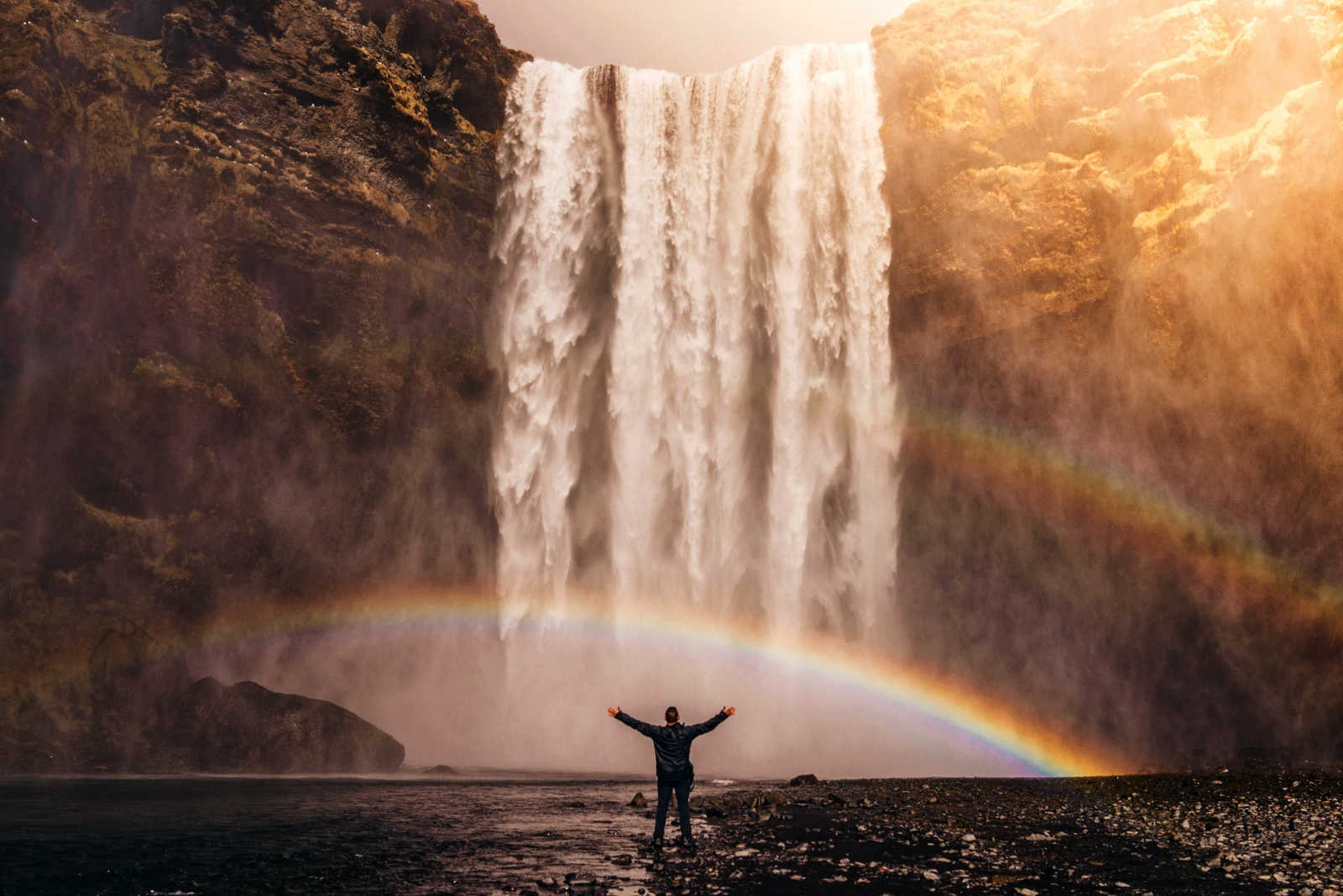 A man standing beneath a waterfall casting a rainbow