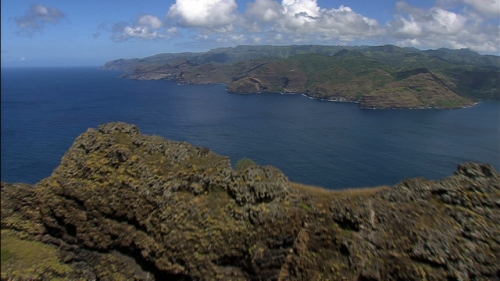 Cinematic aerial shot flying over a mount and discovering the coast of Nuku Hiva, Marquesas islands in french Polynesia