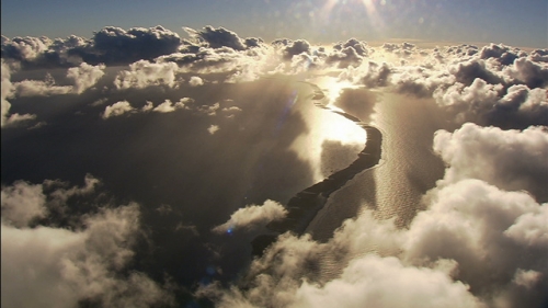 Aerial shot of an atoll and clouds under the sunset light, Tuamotus archipelago in frenc Polynesia