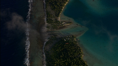 Vertical aerial Shot of the reef, coconut trees, little pass and atoll under sunset lighting, Tuamotu