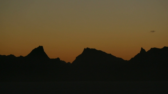 Moorea, panoramic view of sunset on the mountains chain under orange sky, shot from Tahiti