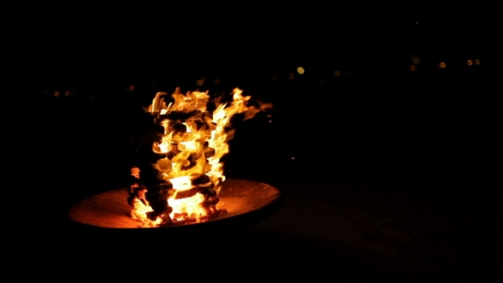 Wood on fire on the beach at night, flames dancing in the wind