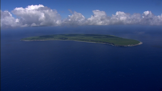 Makatea, aerial view of the island in the ocean, under clouds and blue sky