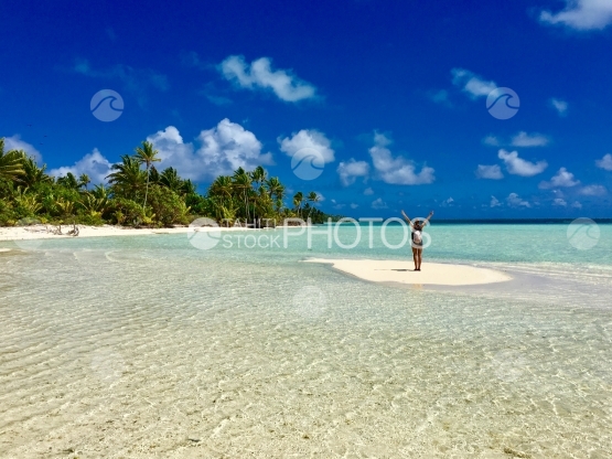 Lady holding arms up in the air on small sand bank in the turquoise water of the lagoon of Tetiaroa