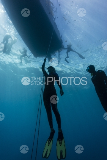 Two free divers training underwater, underneath the boat.