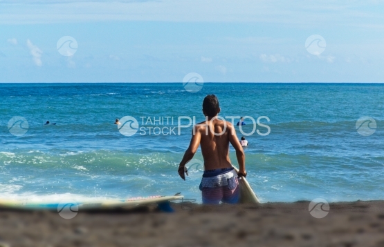 Tahiti, young man going surfing the waves