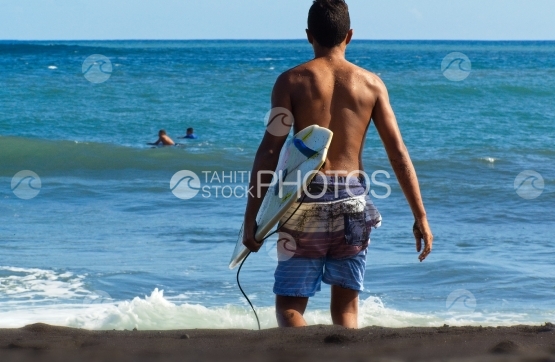 Tahiti, young man going surfing the waves