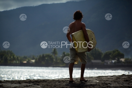 Tahiti, young surfer teenager walking on the black sand beach