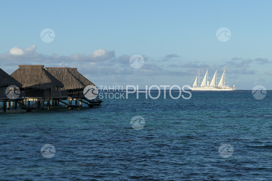 Overwater bungalows in the lagoon, four masts sail boat in the background