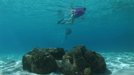 Two snorkelers swimming over a Polynesian sculpture layed on the sand in the lagoon, Moorea