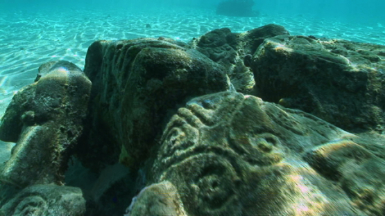 Polynesian sculptures layed on the sand in the lagoon, Moorea
