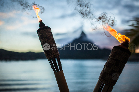 Two Torches in fire with island of Bora Bora in the background during sunset