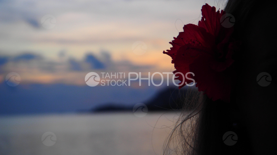 Woman looking at the lagoon at the sunset, hibiscus flower on ear