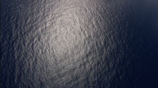 Aerial view over the ocean with sun reflection