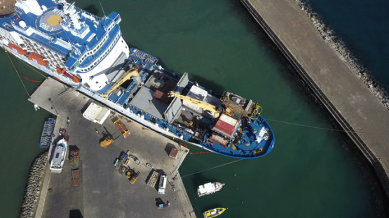 Ua Pou, aerial drone video above a cargo ship unloading goods on the dock, marquesas islands, polynesia, 4K UHD