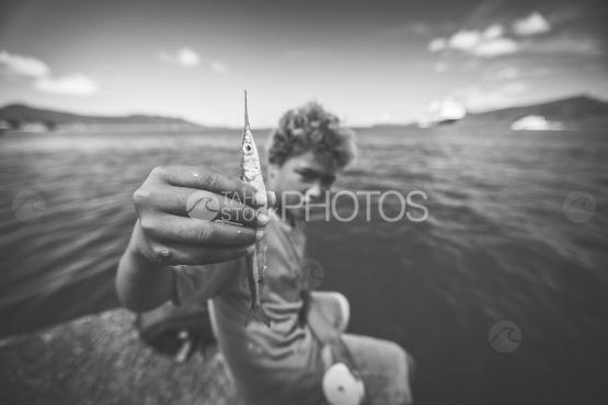 Bora Bora, young fishing boy and needle fish by the lagoon