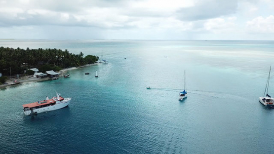 Aerial view by drone of atoll and sail boats anchored in the lagoon, 4K UHD