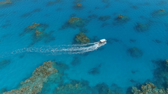 Tubuai, aerial view of a motor boat navigating among the coral reef in the lagoon, 4K UHD