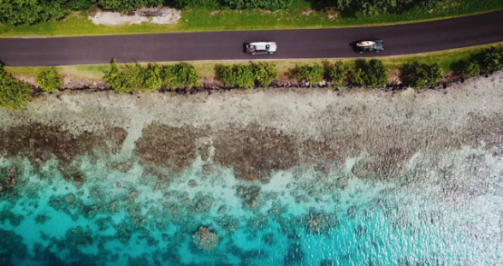 Huahine 4K drone, aerial view of 2 cars on a road in front of the lagoon